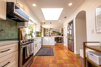 Bright ADU kitchen with terracotta tile flooring, white cabinets, stainless steel appliances, and a large skylight overhead.