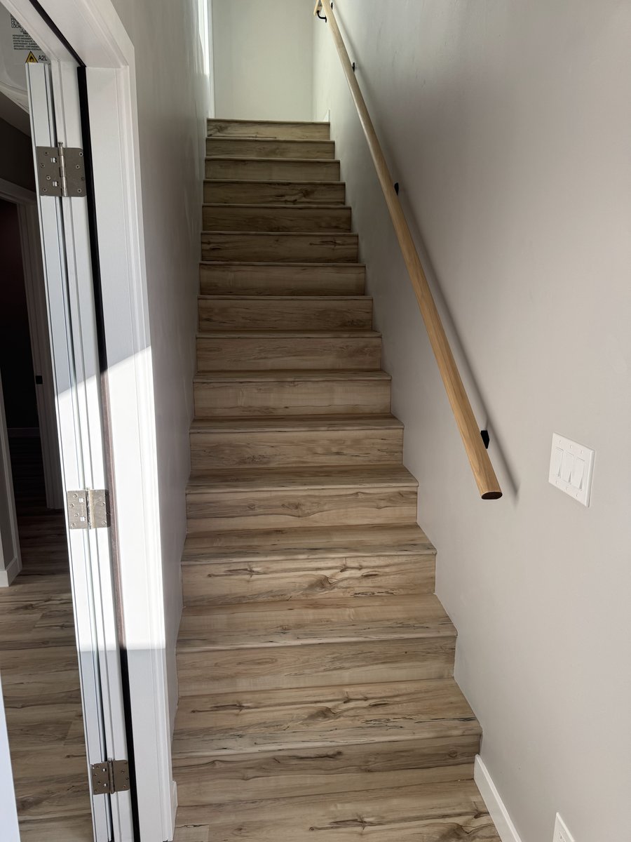 Straight staircase with wood-look LVP treads, gray walls, and a simple wood handrail leading up to a second level.