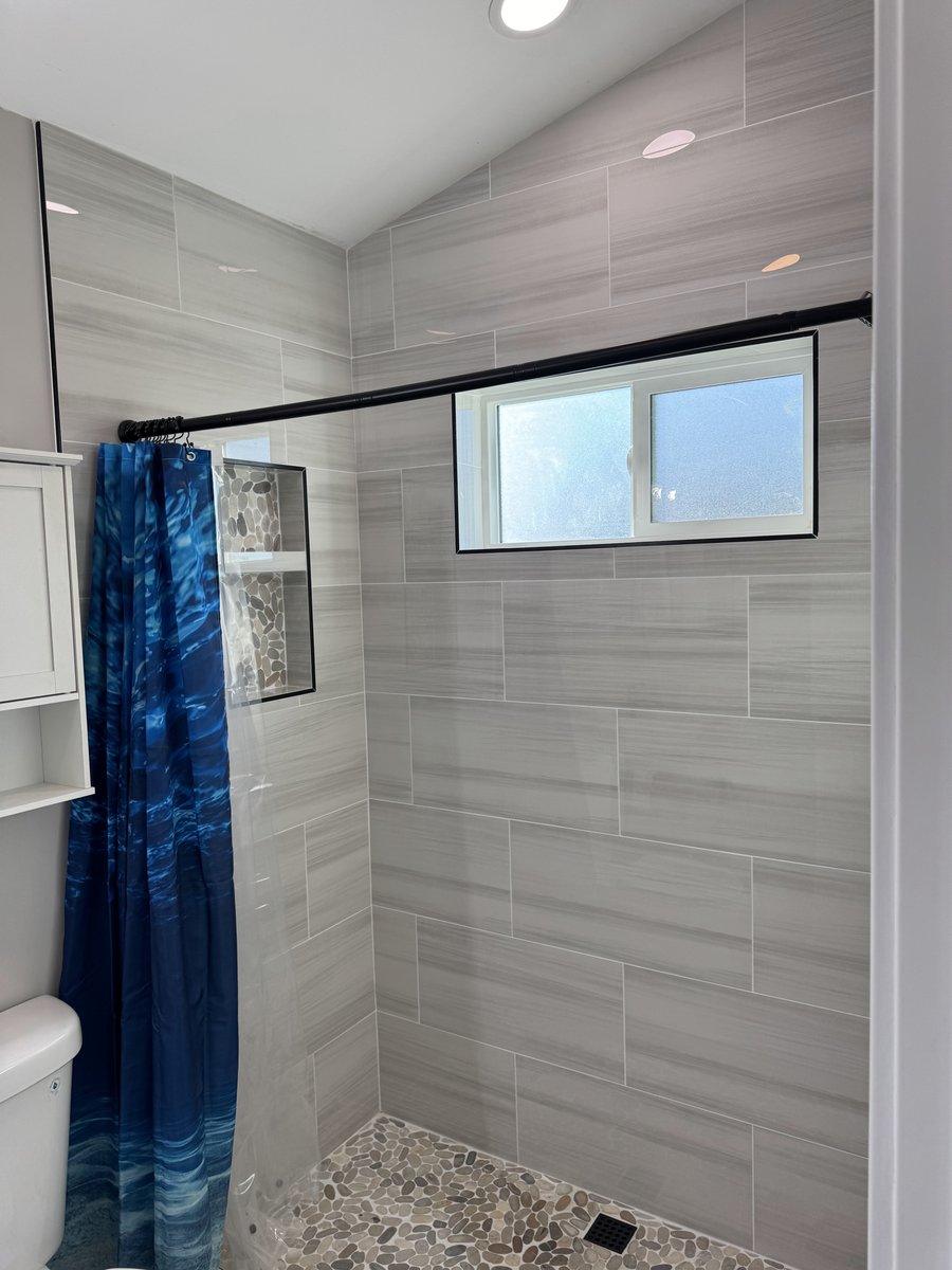 ADU bedroom corner showing a walk-in closet with open shelving, a mirrored sliding door, wood-look flooring, and a window with dark curtains.