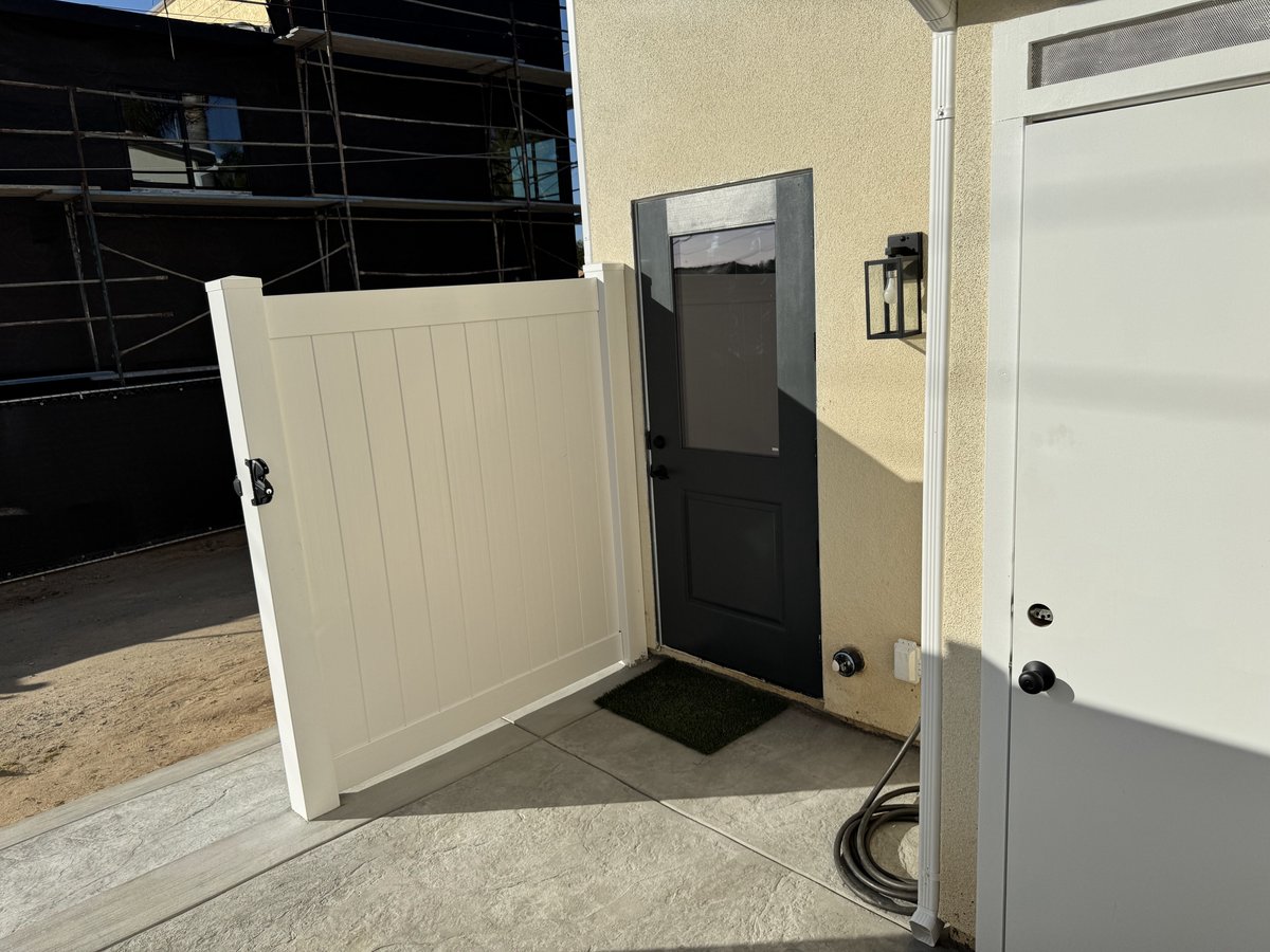 Finished ADU side entrance with vinyl fencing, concrete patio, and exterior lighting