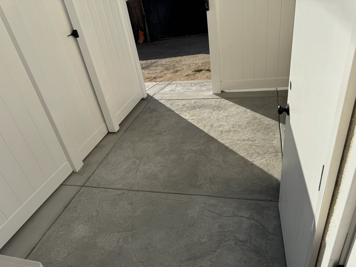 Stamped concrete path leading through white vinyl fence gate toward ADU yard