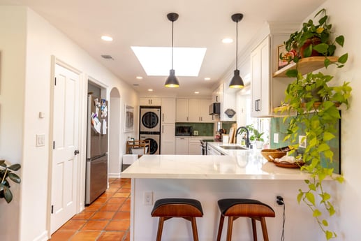 A well-lit kitchen with white cabinets and a marble island featuring two leather bar stools.