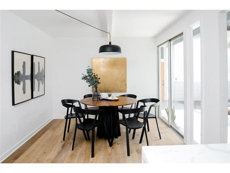 A contemporary dining area with a round wooden table and black chairs, a large pendant light overhead, and an abstract diptych on the wall.




