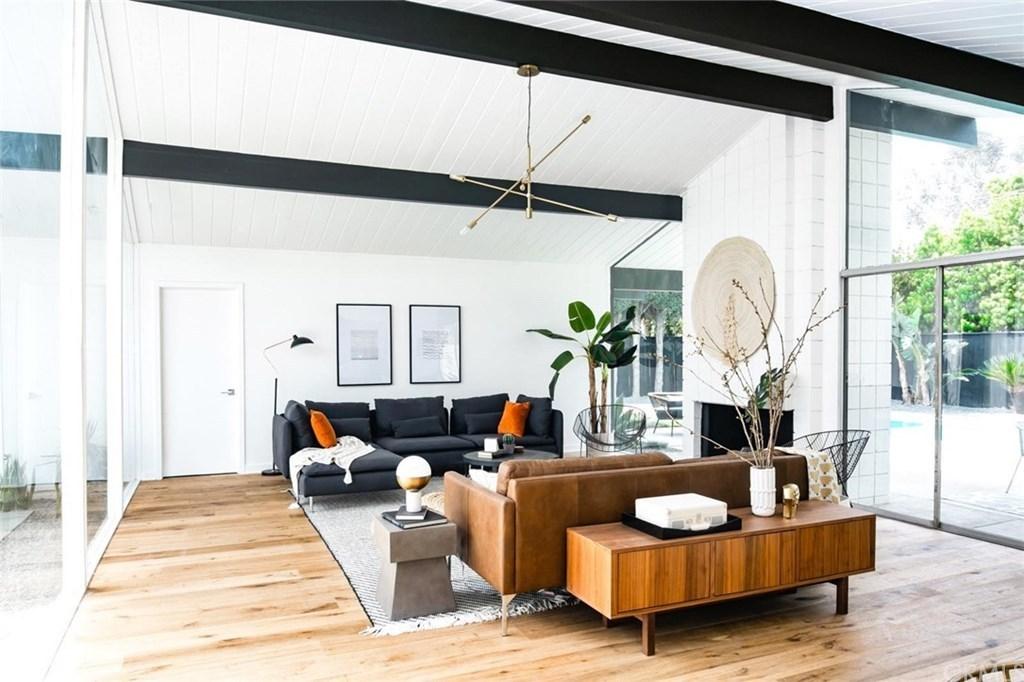 A spacious living area with vaulted ceilings, a dark blue sofa with orange accents, a mid-century wooden coffee table, and a white armchair.