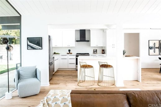 An open-concept living space with a modern interior. The foreground shows a part of a living area with a gray armchair and a brown leather sofa.