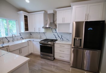 Modern ADU kitchen with white shaker cabinets, marble-look backsplash, stainless steel stove and refrigerator, and light wood flooring.