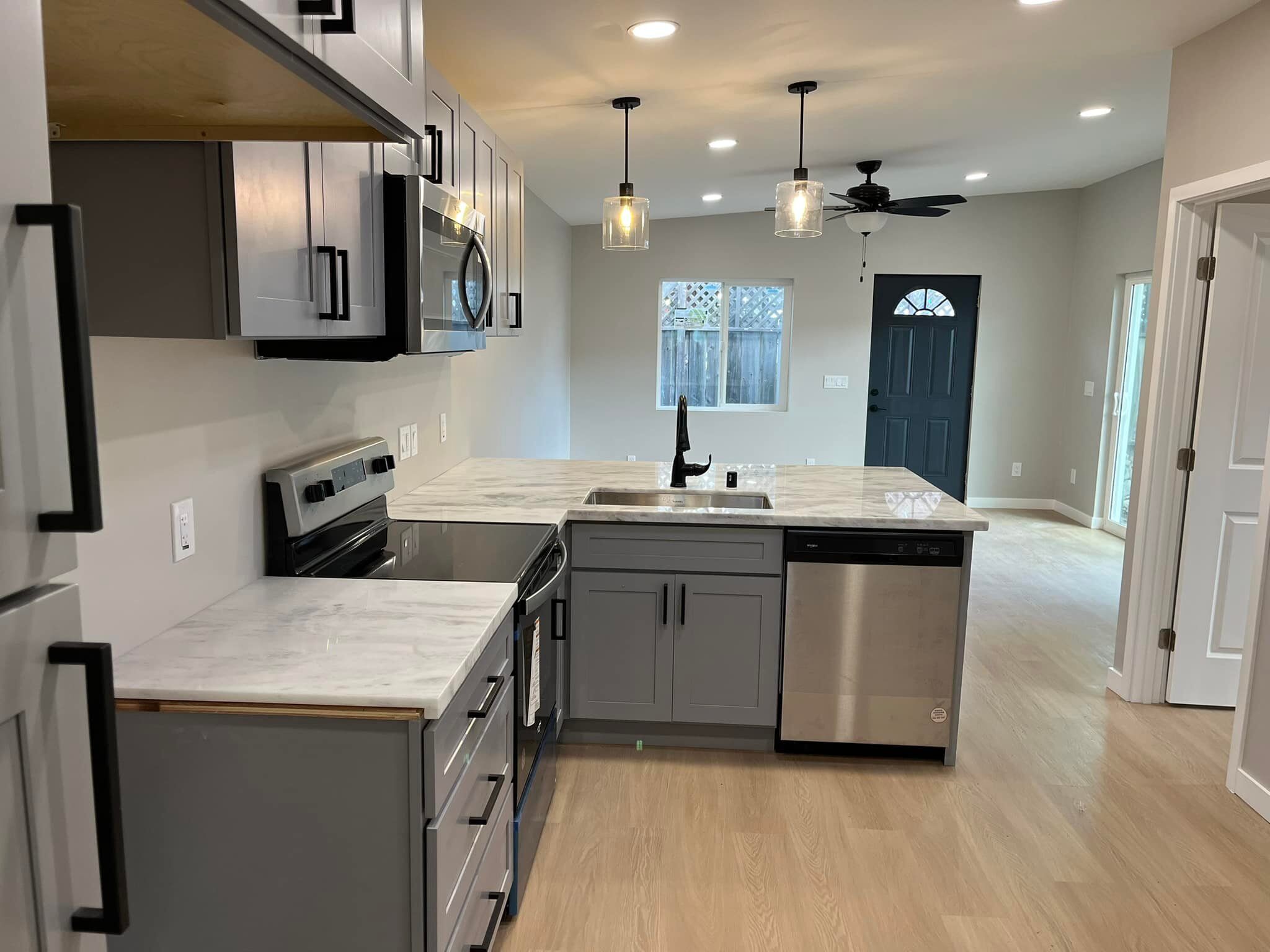 Modern ADU kitchen with gray cabinets, white quartz countertops, stainless steel appliances, and an open layout leading to a dark front door.