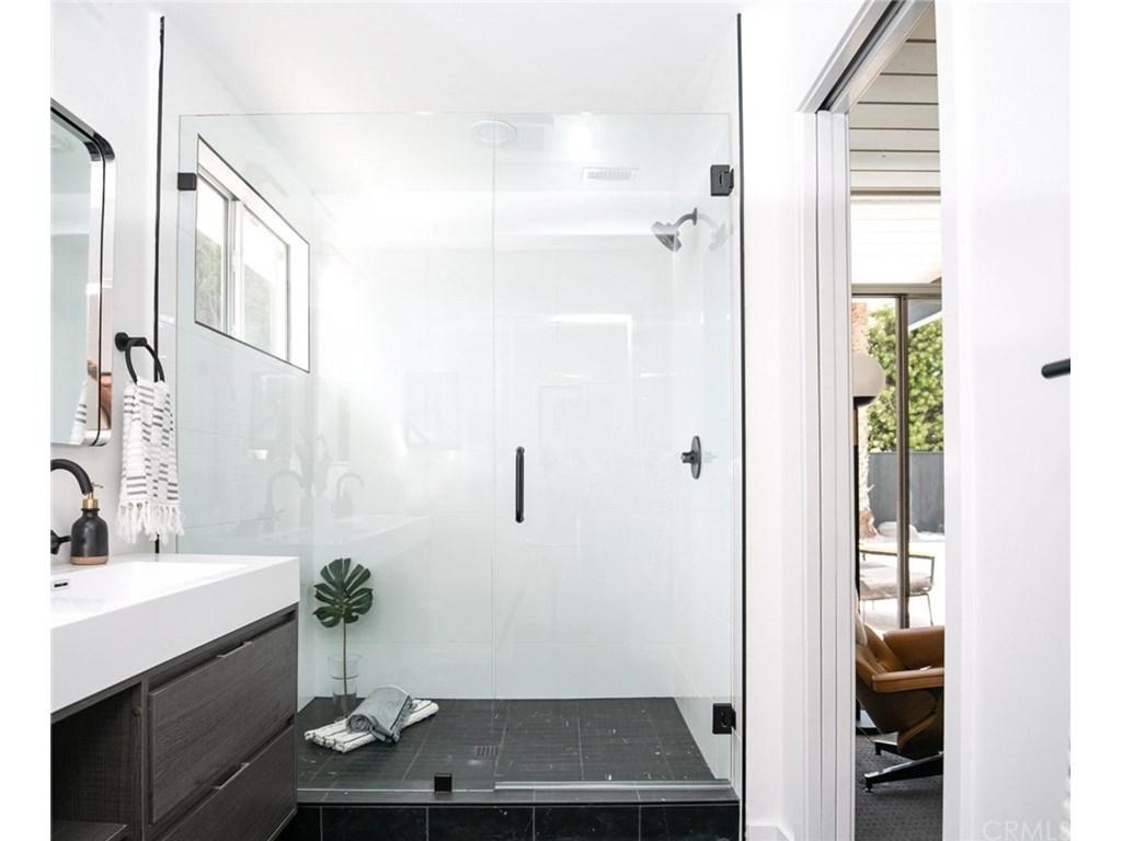 A modern bathroom with a large walk-in shower featuring clear glass doors, black fixtures, a dark tiled floor, and a vanity with a white countertop.