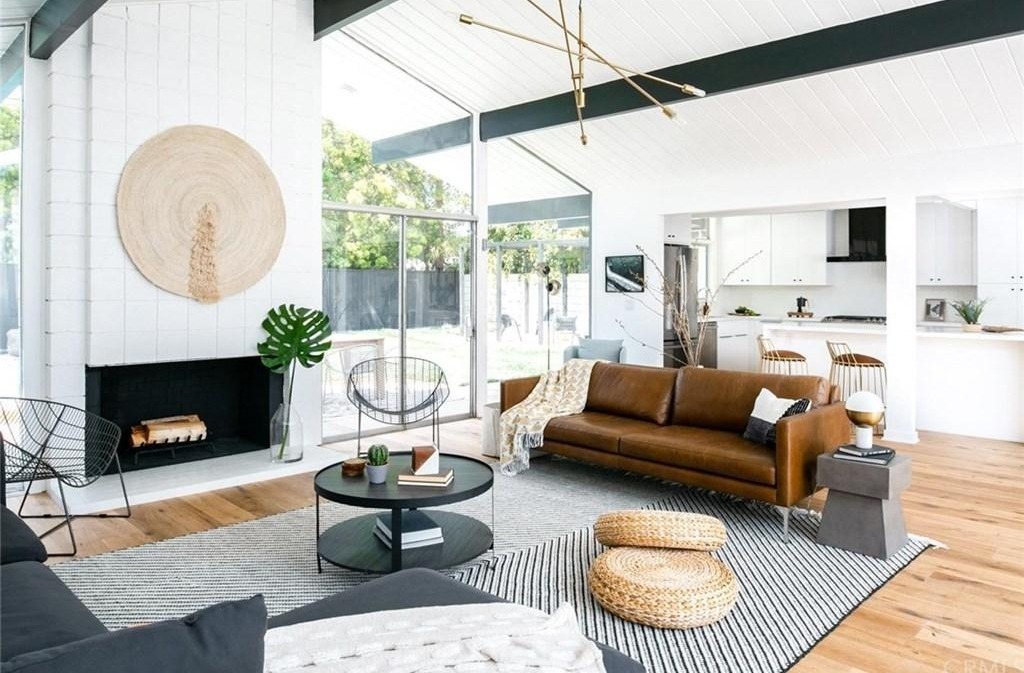 A spacious living room with a high white ceiling and exposed black beams, featuring a brown leather sofa, black accent chairs, and a modern black coffee table.